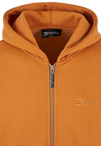 Haut de sweatshirt zippé orange avec une grande capuche, comportant un nom de marque brodé "Dropsize" et une fermeture éclair métallique. Texture de tissu lisse.