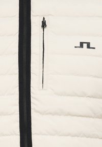 Krém színű pufi kabát fekete cipzárral és logóval. Steppelt textúrájú, bal oldalon cipzáros zsebbel rendelkezik.