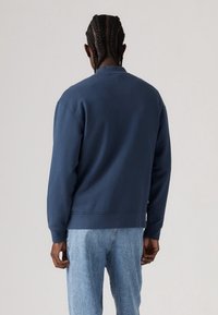 Sudadera azul marino con cuello redondo y mangas largas, con un corte relajado y puños acanalados, combinada con jeans de denim claros.