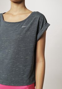 Grå kortärmad sporttop med rund halsringning, med ett subtilt mönster och en liten reflexande Nike-logotyp på bröstet.