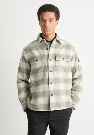 Groen en beige geruite flanellen jas met knoopsluiting aan de voorkant, twee borstzakken en zwarte knopen. Zachte textuur en casual ontwerp.