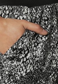 Gonna a strisce bianco e nere con una mano visibile che inserisce in una tasca laterale. Il tessuto sembra texturizzato con dettagli di vita elastica.