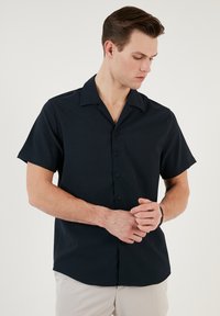 Rövid ujjú, sötétkék gombos ing sima anyagból, klasszikus gallérral és diszkrét, lekerekített aljjal. Nincs látható minta.