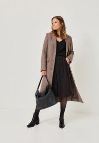 Hnědý vlněný kabát, černý top, černá plisovaná sukně, černé punčocháče a špičaté černé kotníkové boty. Černá kožená kabelka přes rameno, hladká textura.