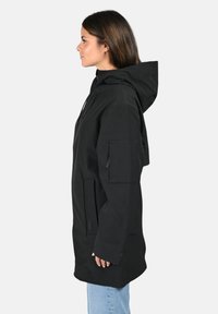 Giacca lunga nera con cappuccio, realizzata in materiale liscio. Presenta tasche frontali e una tasca laterale, mostrata dal profilo sinistro.