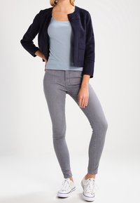 Marinblå cropped jacka, ljusblå prickig tanktop, grå slim jeans och vita sneakers. Slät tyg med modern passform och minimala detaljer.