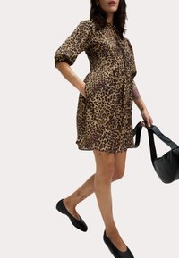 Robe à imprimé léopard avec des manches bouffantes courtes, taille cintrée et poches latérales, associée à des ballerines noires et un sac à bandoulière noir.