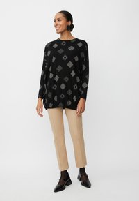 Schwarzes Langarmoberteil mit geometrischen silbernen Mustern, kombiniert mit beigen Slim-Fit-Hosen und schwarzen Riemchenschuhen. Glattes, leichtes Material.