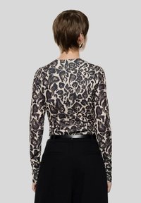 Top a maniche lunghe con motivo a stampa leopardata in tonalità beige e marrone, realizzato in tessuto liscio, abbinato a pantaloni neri e una cintura sottile.