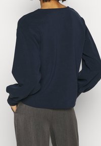 Mörkblå sweatshirt med avslappnad passform, rundad halsringning och puffärmar, i kombination med grå skräddarsydda byxor. Mjuk textur, minimalistisk design.