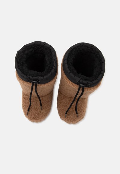 Ζευγάρι καφέ παντόφλες με επένδυση fleece και μαύρα κορδόνια στον αστράγαλο, σε άνω όψη σε λευκό φόντο.