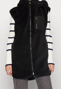 Czarna bezrękawnikowa kamizelka z puszystej tkaniny z zamkiem błyskawicznym i kapturem, z małą kieszenią na zamek na piersi i długimi rękawami w paski.