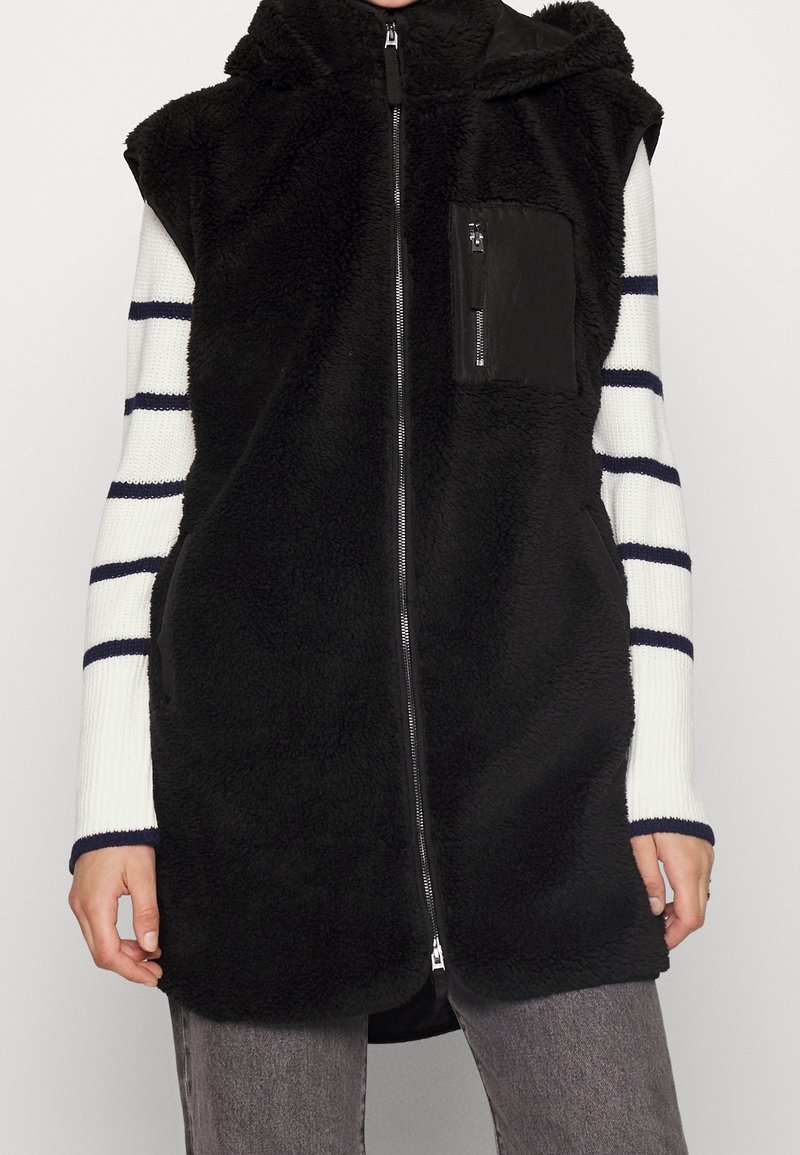 Czarna bezrękawnikowa kamizelka z puszystej tkaniny z zamkiem błyskawicznym i kapturem, z małą kieszenią na zamek na piersi i długimi rękawami w paski.