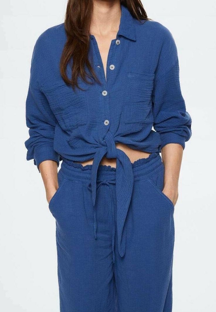 Sininen, teksturoiduilla yksityiskohdilla varustettu napitettava paita, jossa vyötäröllä solmittavat nauhat. Yhdistetty vastaaviin narusolmullisiin housuihin, joissa on sivutaskut ja joustava vyötärö.