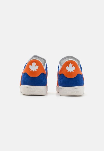Zapatillas de ante azul con acentos naranjas, que presentan un diseño de hoja de arce blanca en el talón, forro gris y suela de goma blanca.