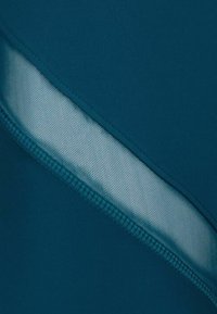 Tejido deportivo en color azul verdoso con un inserto de malla texturizada a lo largo de una costura en diagonal; cuenta con un acabado suave y costuras reforzadas.