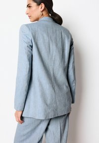 Lyseblå skræddersyet blazer med lange ærmer, en glat tekstur og struktureret design. Har en ventileret ryg og minimale syninger.