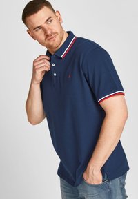 Navyblauw polo shirt van katoen met een rood en wit gestreepte kraag. Voorzien van drie knoppen en een klein logo op de borst.