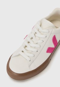 Hvite lær sneakers med rosa detaljer, rund tå, syddi detaljer, og brun gummisåle. Har tradisjonell snøring.