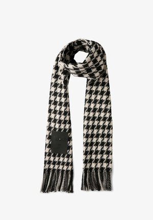 Bufanda con patrón de houndstooth en blanco y negro hecha de un tejido suave, con bordes con flecos y un parche negro con el logo que dice "desde 1995".