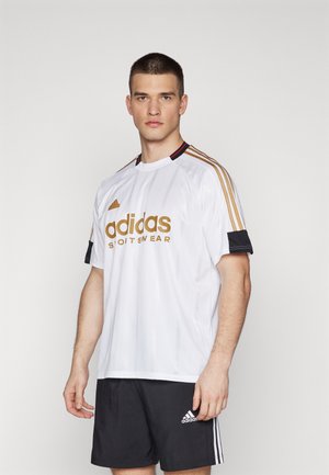 Biała sportowa koszulka Adidas z złotym logo, czarnymi rękawami oraz trzema złotymi paskami na ramionach, w komplecie z czarnymi szortami.