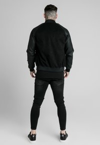 Svart bomberjacka med mockakropp och svarta lädersleeves. Ribbad mudd och nederkant. Bärs med svarta jeans och sneakers. Enfärgad grå bakgrund.