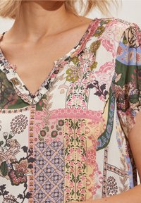 Bluzka z krótkim rękawem z dekoltem w serek, wykonana z lekkiego materiału w kolorowy wzór patchworkowy z motywami kwiatowymi i geometrycznymi.