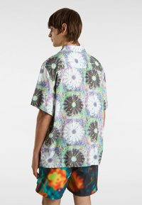 Camicia a maniche corte con un vivace motivo floreale in bianco e nero, su uno sfondo astratto multicolore. Realizzata in tessuto leggero.