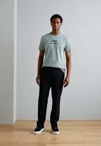 Lichtblauwe katoenen t-shirt met zwart logo, gecombineerd met zwarte broeken en zwarte sneakers. Glad materiaal, casual pasvorm, minimalistisch ontwerp.