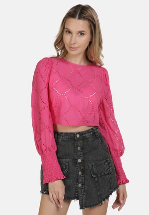 Kvinde iført en lyserød langærmet crop-top med hulmønster og en højtsiddende sort denim mininederdel med knapper foran og lommer.