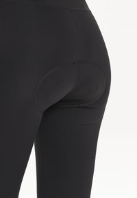 Zwarte sportleggings met een aansluitend ontwerp, een gladde textuur en een opvallende uitsnijding op de rug. Verstevigde naden zijn zichtbaar.
