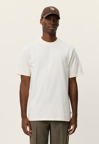 Λευκό βαμβακερό μπλουζάκι με κοντά μανίκια και στρογγυλή λαιμόκοψη, με εμπρόσθια τσέπη με υφή, συνδυασμένο με καφέ καπέλο μπέιζμπολ.