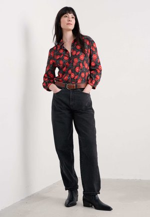 Camicia a maniche lunghe con bottoni a fiori rossi su sfondo scuro, abbinata a jeans neri a vita alta e stivaletti neri. Compreso una cintura marrone.