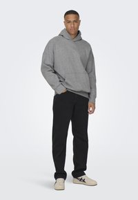 Grauer Kapuzenpullover mit einer Kängurutasche, kombiniert mit schwarzen Jeans und beigen Sneakers mit dunkelblauen Akzenten.