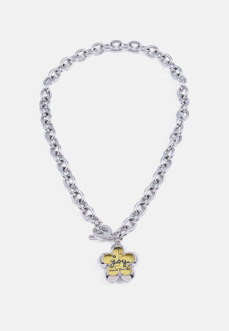 Collier en chaîne argentée épaisse avec un charme en forme de fleur à cinq pétales, comportant un fond jaune et un texte en cursive noire.