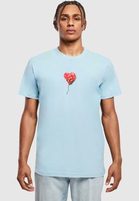Světle modré tričko s krátkým rukávem, které na středu obsahuje grafiku červeného balónku ve tvaru srdce se bílými květinovými akcenty. Vyrobeno z měkké bavlny.
