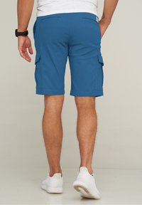 Blaue Cargo-Shorts mit einer glatten Textur, zwei Seitentaschen und zwei Gesäßtaschen, kombiniert mit weißen Sportschuhen.