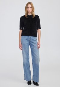 Czarny puszysty sweter z krótkim rękawem ozdobiony koralikami, w połączeniu z jasnoniebieskimi dżinsami o szerokich nogawkach z postrzępionymi brzegami i wysokim stanem.