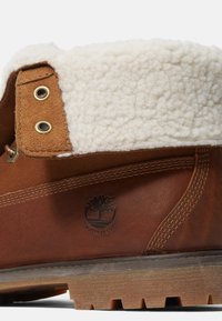 Braune wasserdichte Stiefel mit einem weichen weißen Fleece-Kragen, strukturiertem Lederkörper, Messing-Ösen und einer robusten Sohle mit Grip-Mustern.