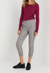 Bordowy sweter z długim rękawem w połączeniu z szarymi spodniami 3/4 w kratę i czarnymi sneakersami. Gładki materiał, dopasowany krój i elastyczny pas.
