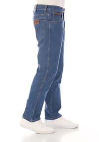 Jeans in denim blu con vestibilità dritta, caratterizzati da una toppa in pelle sul retro, dettagli cuciti e tasche laterali.