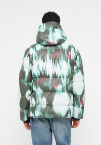 Padded bunda s kapucňou; má farebný abstraktný vzor v odtieňoch teal, šedej a ružovej. Vyrobená z lesklého, hladkého materiálu.