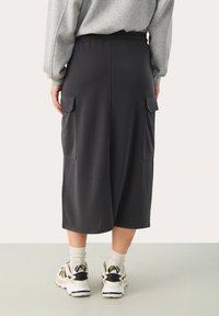 Donkergrijze midi-rok van zachte stof, met een relaxte pasvorm, zijzakken en een comfortabele elastische tailleband. Gecombineerd met sneakers.