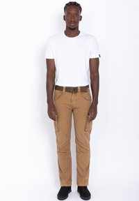 Witte t-shirt met korte mouwen gecombineerd met tan cargo pants met zijzakken en een bruine riem. Zwarte sneakers maken de outfit compleet.
