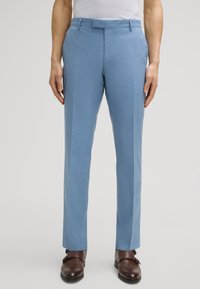 Hellblaue Anzughose aus strukturiertem Stoff, mit flacher Vorderseite, Gürtelschlaufen und slim-fit Design. Getragen mit braunen Schuhen.