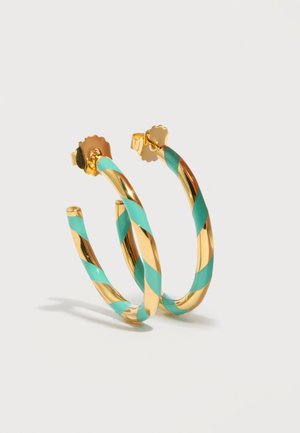 Gouden creolen gedraaid met turquoise strepen, bevestigd met gegolfde vlinderruggen, weergegeven tegen een effen lichte achtergrond.