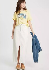 Żółta koszulka graficzna z napisem "Najlepszy", biała dżinsowa spódnica maxi z przodem rozciętym, beżowe sandały na platformie oraz niebieska dżinsowa kurtka.