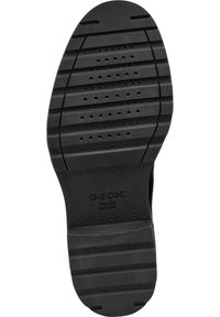 Suela de zapato de goma negra con estrías texturizadas, perforaciones circulares y una impresión de logo. Diseñada para ofrecer agarre y transpirabilidad.