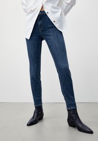 Tunna blå jeans i denim med en klassisk femficksdesign, med en subtil blekning och en smidig yta. Bärs med svarta ankelstövlar.