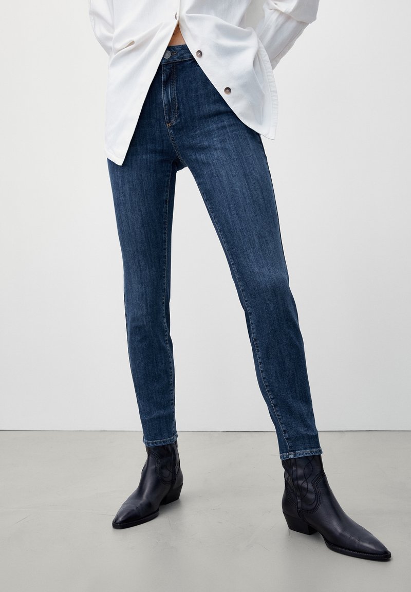 Tunna blå jeans i denim med en klassisk femficksdesign, med en subtil blekning och en smidig yta. Bärs med svarta ankelstövlar.